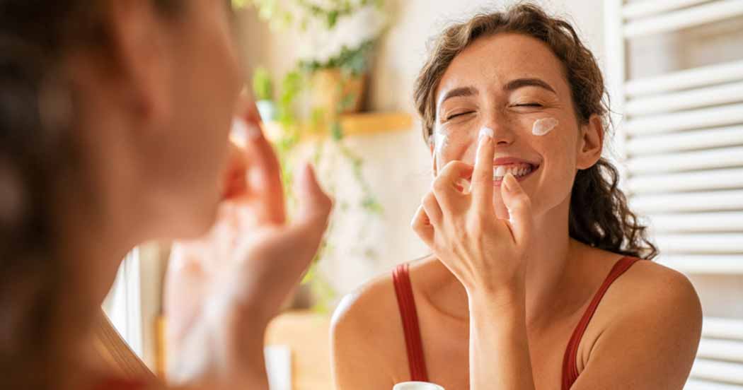 woman putting cream on her face while smiling